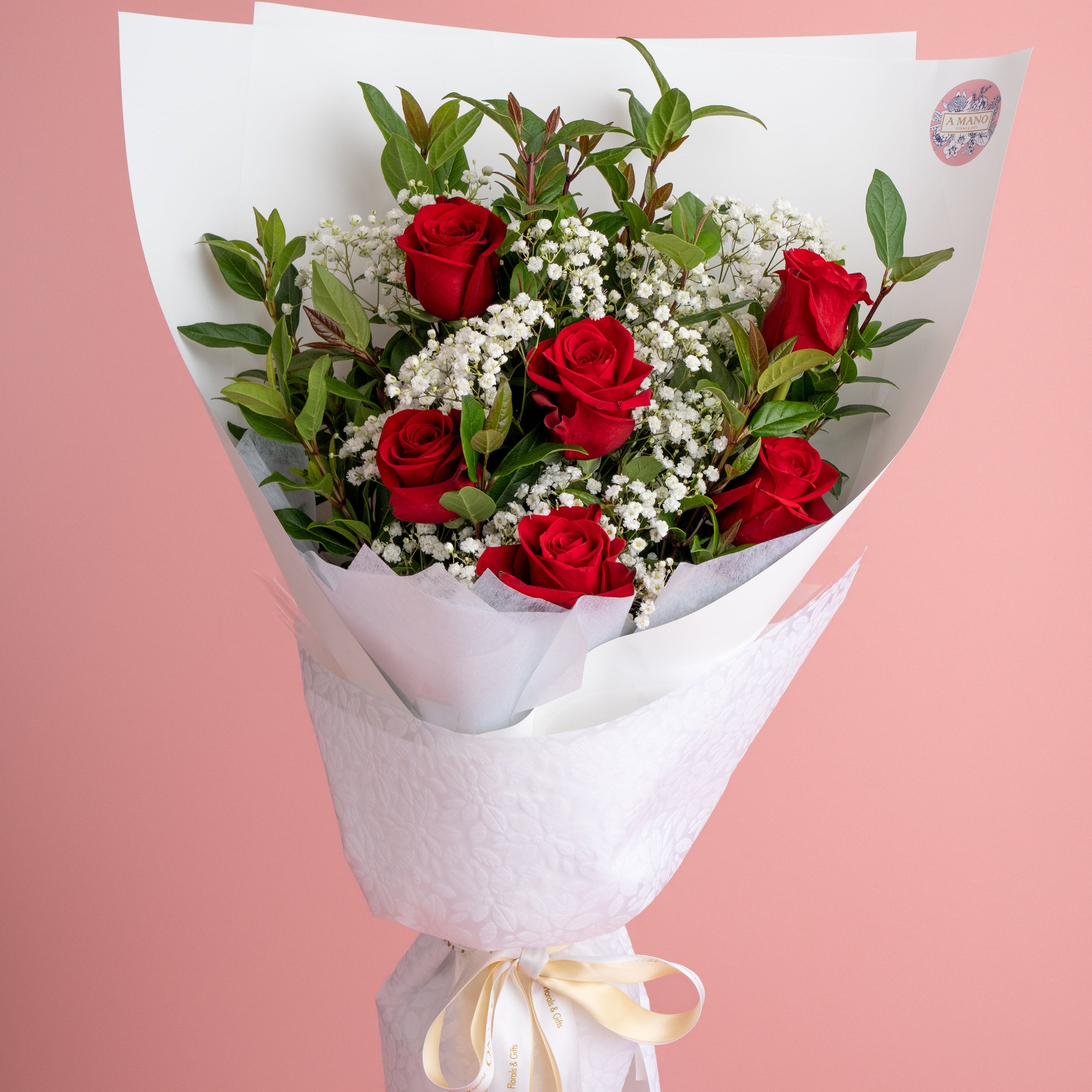 Bouquet of red roses and white flowers wrapped in white paper with a yellow ribbon on a pink background