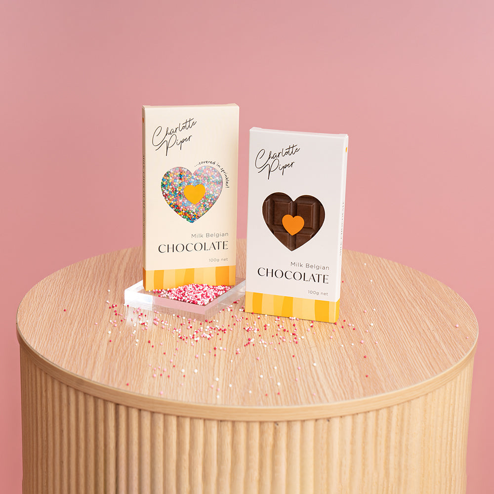 Charlotte Piper chocolate gift bars – milk and dark – styled for a luxury flower hamper, on pink background.